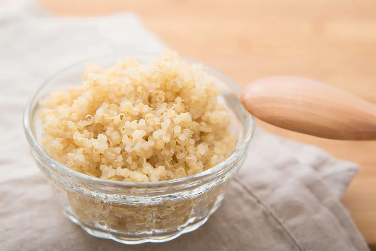 A transparent bowl of cooked quinoa with wooden spoon | Girl Meets Food