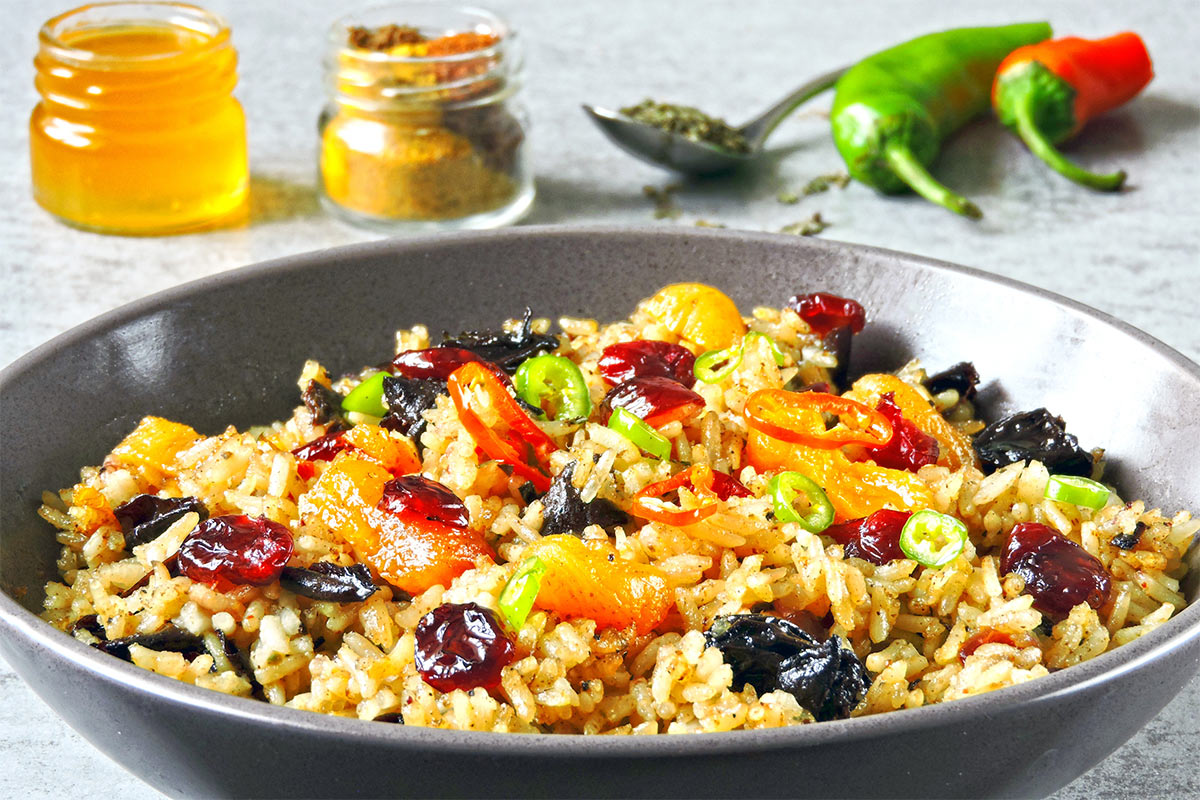 Grey bowl of biryani is on a grey surface. There are some spices and chili peppers next to it | Girl Meets Food