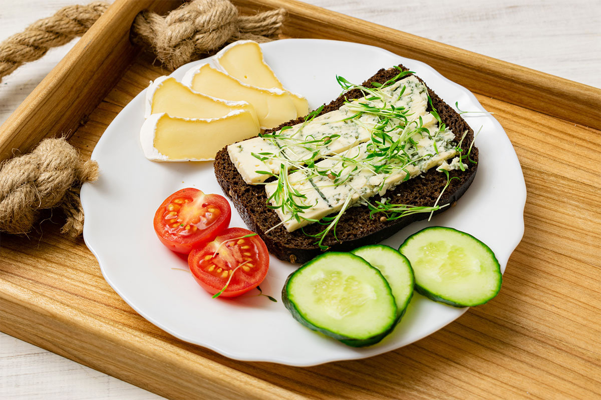 A plate with brie sandwich, brie slices, two tomato halves, cucumber slices is on a wooden tray | Girl Meets Food