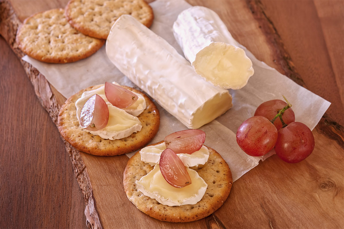 A few crackers, grapes and brie cheese are on a wooden board | Girl Meets Food
