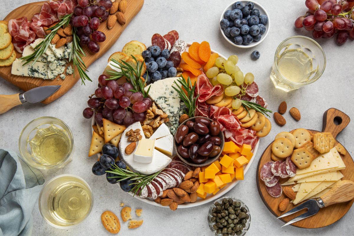 Three charcuterie boards on a white surface. There are some glasses and fruit next to them | Girl Meets Food