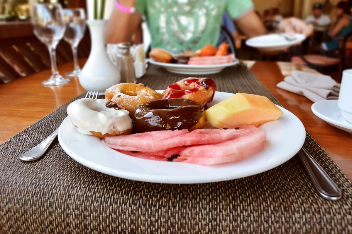 A big plate of donut breakfast is on a table. There is cutlery next to it. A person sits on the background | Girl Meets Food