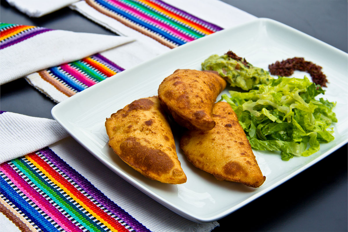 A rectangle plate with three empanadas and salad is on the black table. White towels with colorful stripes lie near the plate  | Girl Meets Food