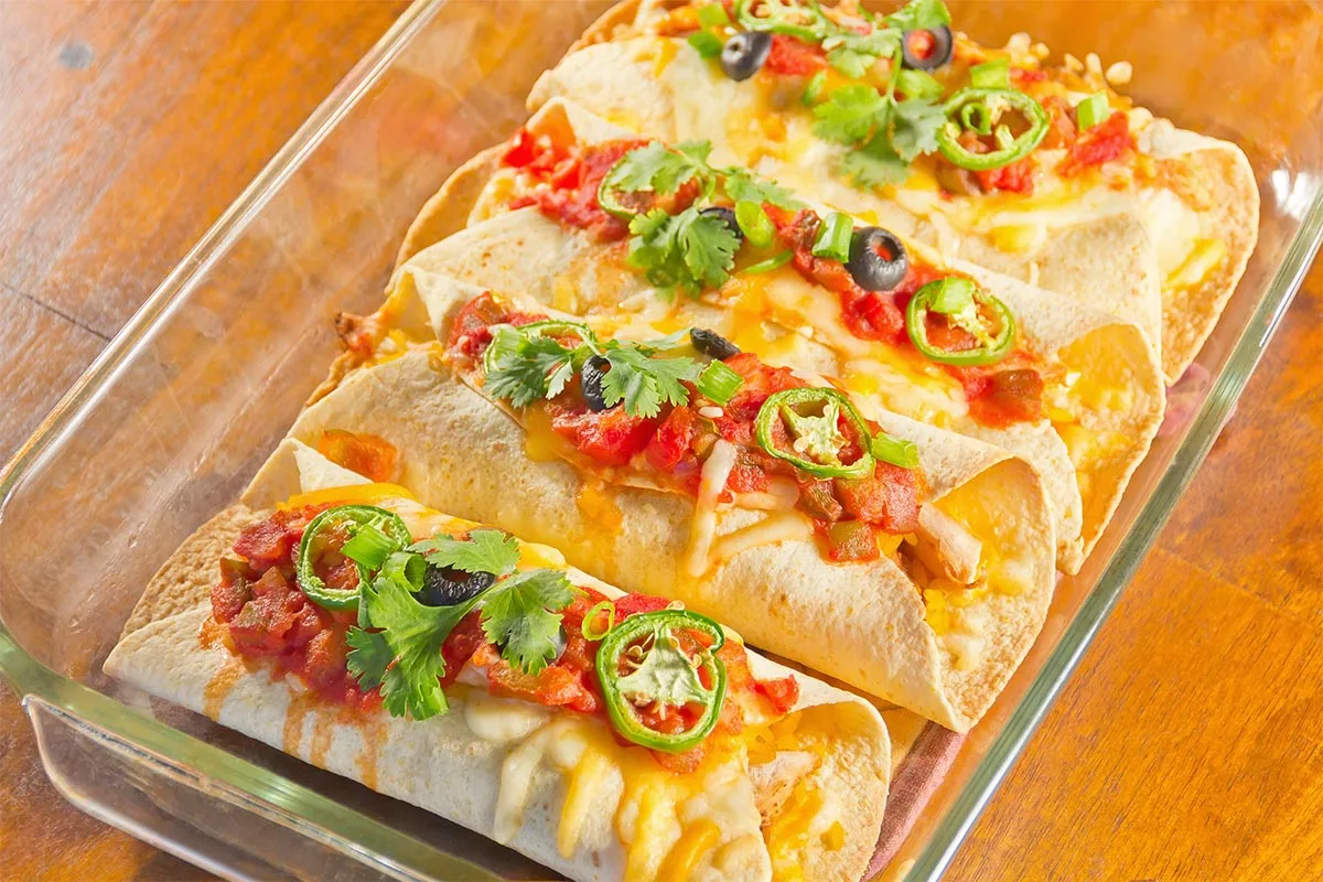 A transparent baking dish with enchiladas casserole is on a table | Girl Meets Food
