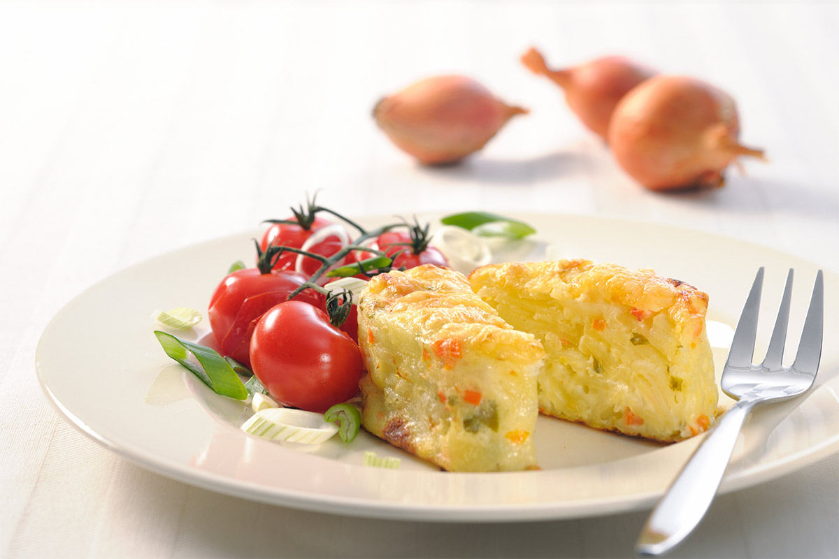 A plate of cheese souffle with cherry tomatoes and a fork is on a table. There are 3 onions next to the plate | Girl Meets Food