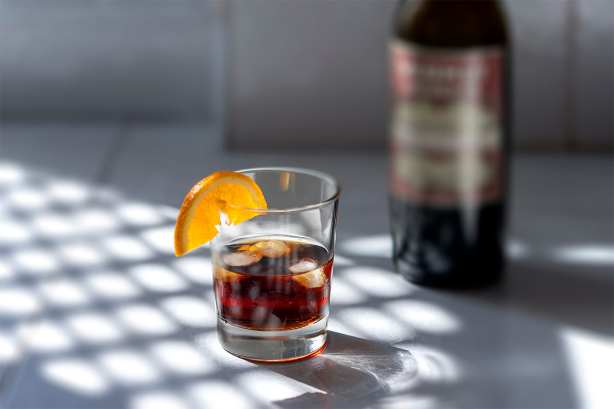 A glass of vermouth with ice cubes and a slice of orange | Girl Meets Food