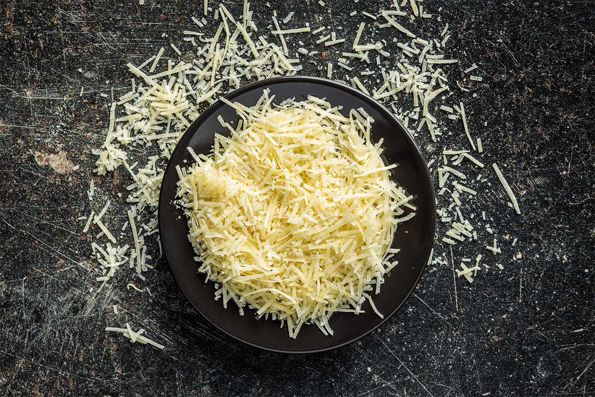 A black plate of grated Parmesan cheese is on a black surface | Girl Meets Food