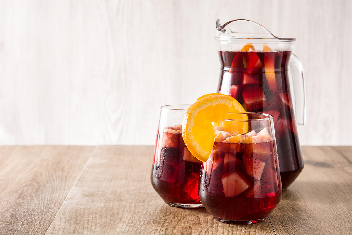 A jug of sangria and two glasses with drink on wooden surface | Girl Meets Food