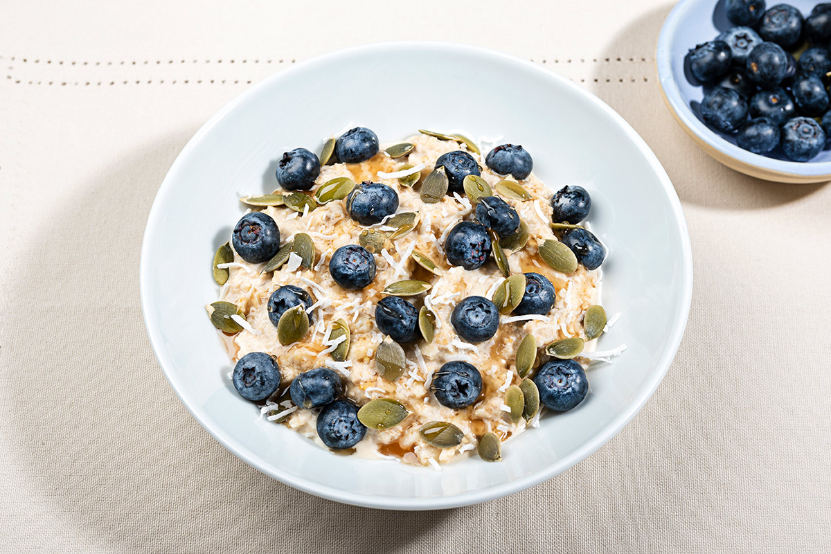 A bowl of Swiss Bircher Muesli topped with pumpkin seeds and blueberries is on the table. There is a small bowl with blueberries next to it | Girl Meets Food