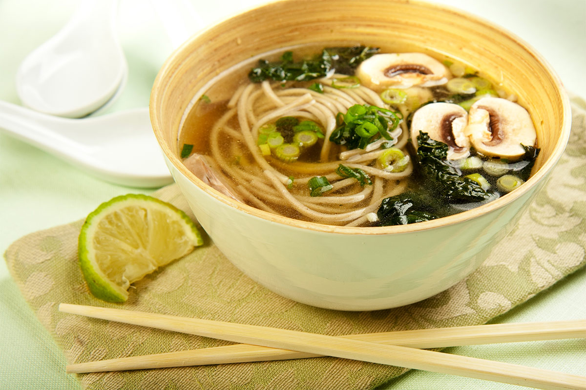 A bowl of soba noodle soup with sticks and a wedge of lemon | Girl Meets Food