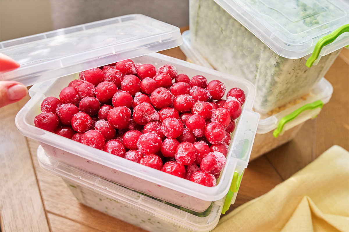 Plastic containers with frozen cherries, peas and corn kernels on the table | Girl Meets Food
