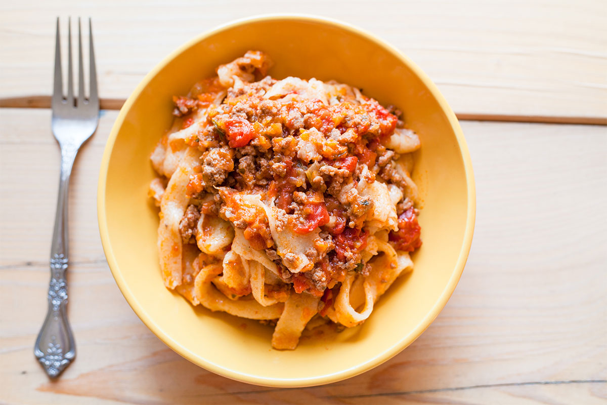 A bowl of Pappardelle bolognese with a fork next to it | Girl Meets Food