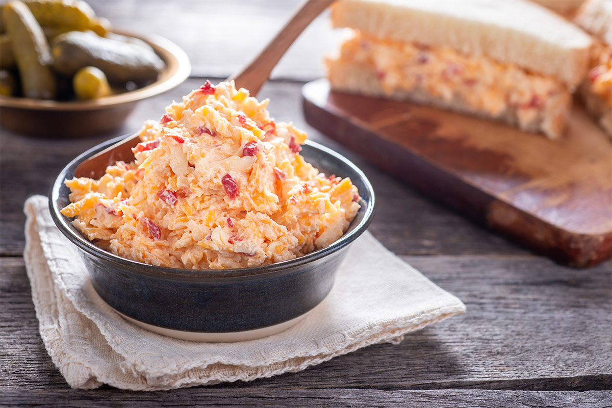 A bowl of pimento cheese is on a towel. There are sandwiches and a bowl pickled cucumbers behind it | Girl Meets Food