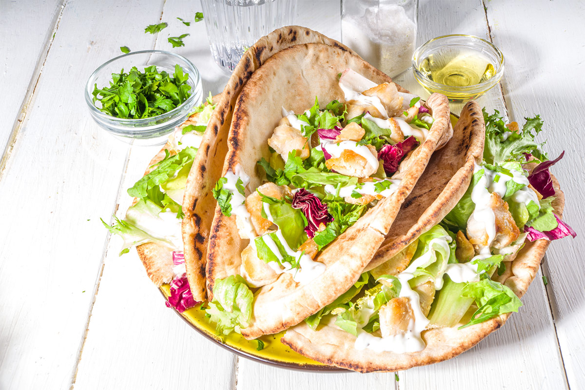 A plate of pita gyro on white wooden surface | Girl Meets Food