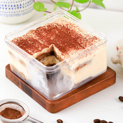 A box of tiramisu on the table. Coffee grains are scattered around it | Girl Meets Food