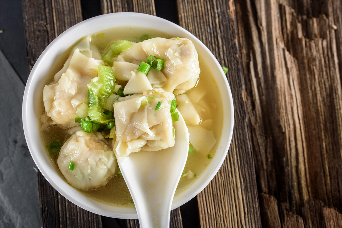 A bowl of wonton soup on wooden table | Girl Meets Food