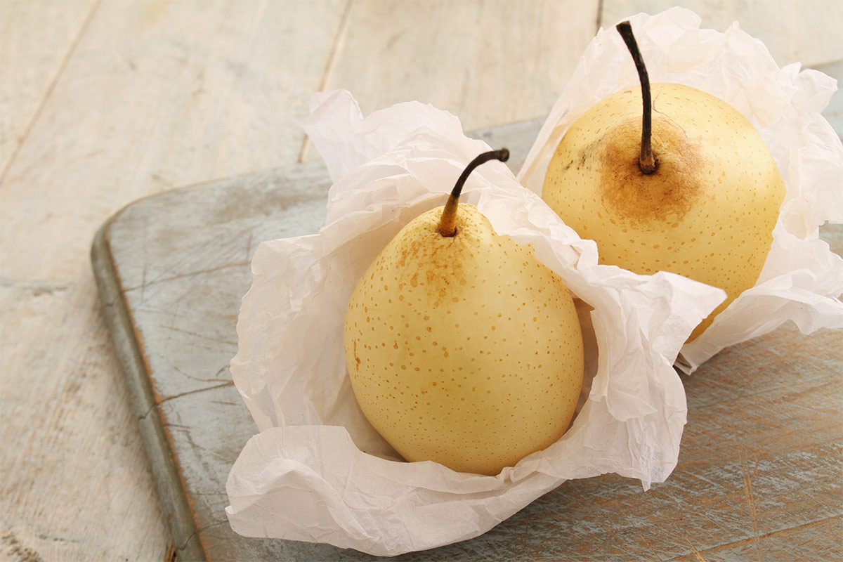 Two yali pears are wrapped in white paper that are on a cutting board | Girl Meets Food