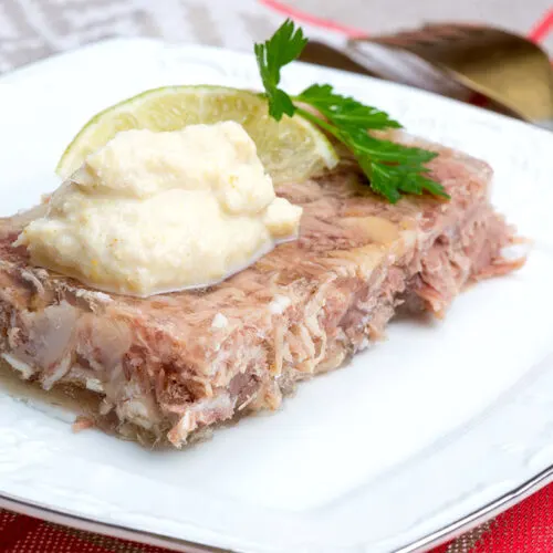 A piece of kholodets topped with chopped horseradish on a plate | Girl Meets Food