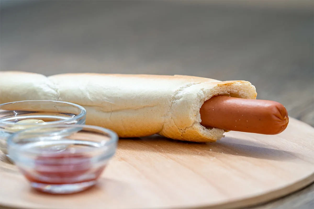 Hot dog in a roll on a wooden board. There are two small transparent bowls next to it | Girl Meets Food