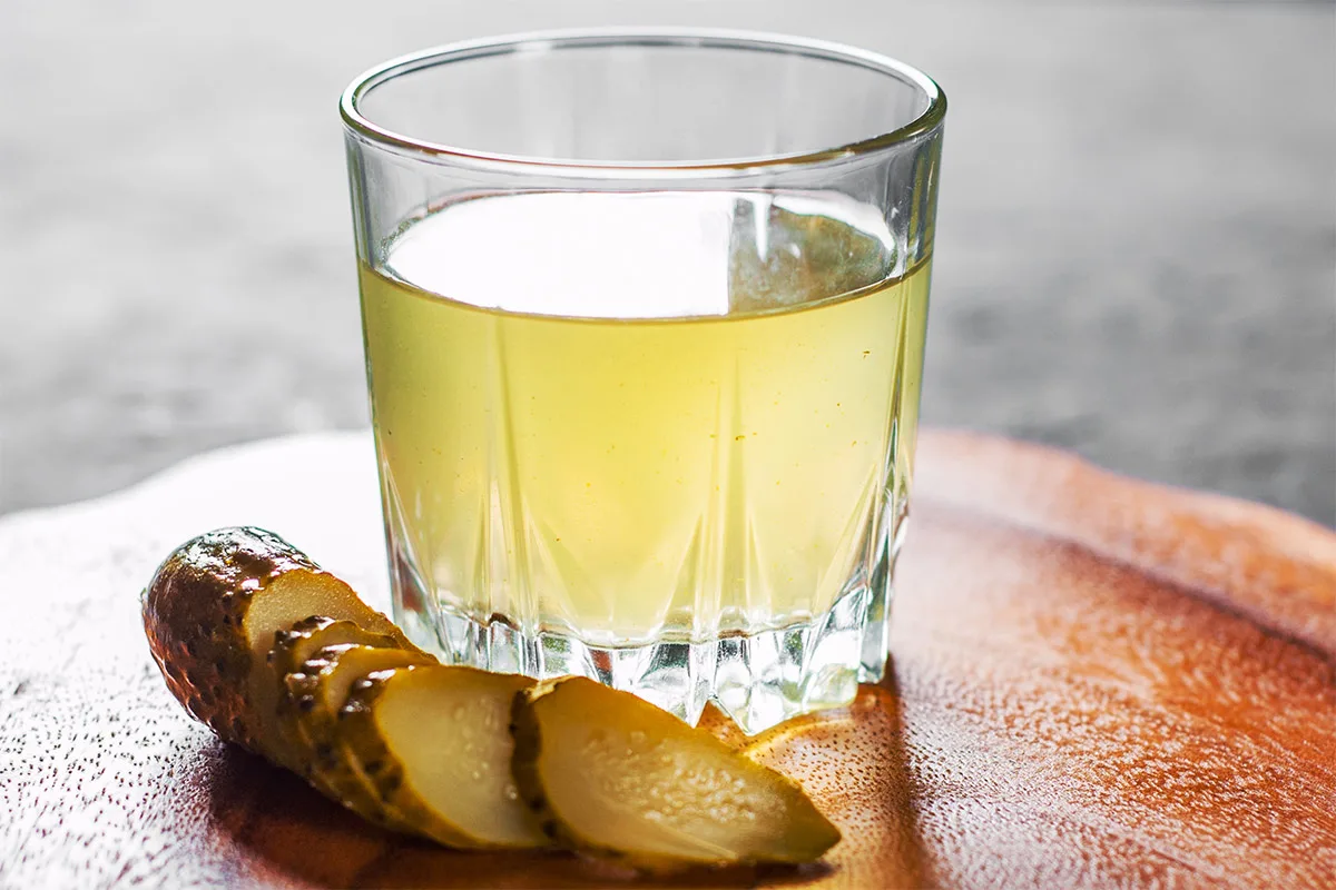 A glass of pickle juice with sliced pickle cucumber on the cutting board | Girl Meets Food