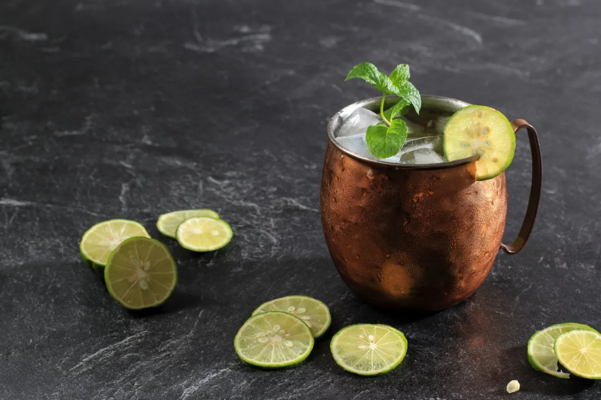 A cup of Kyiv Mule drink on the marble surface. There are lime slices next to it | Girl Meets Food