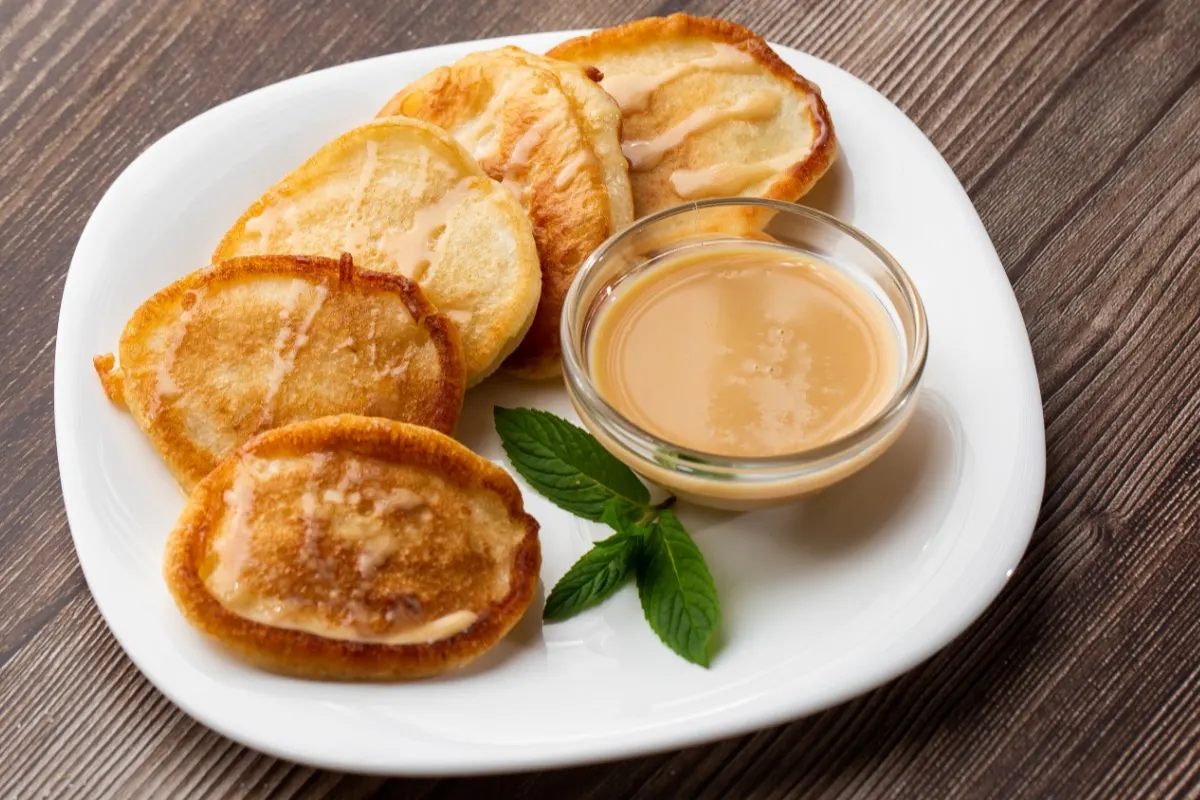 Pile of freshly fried thick pancakes (oladky) with condensed milk on wooden background | Girl Meets Food