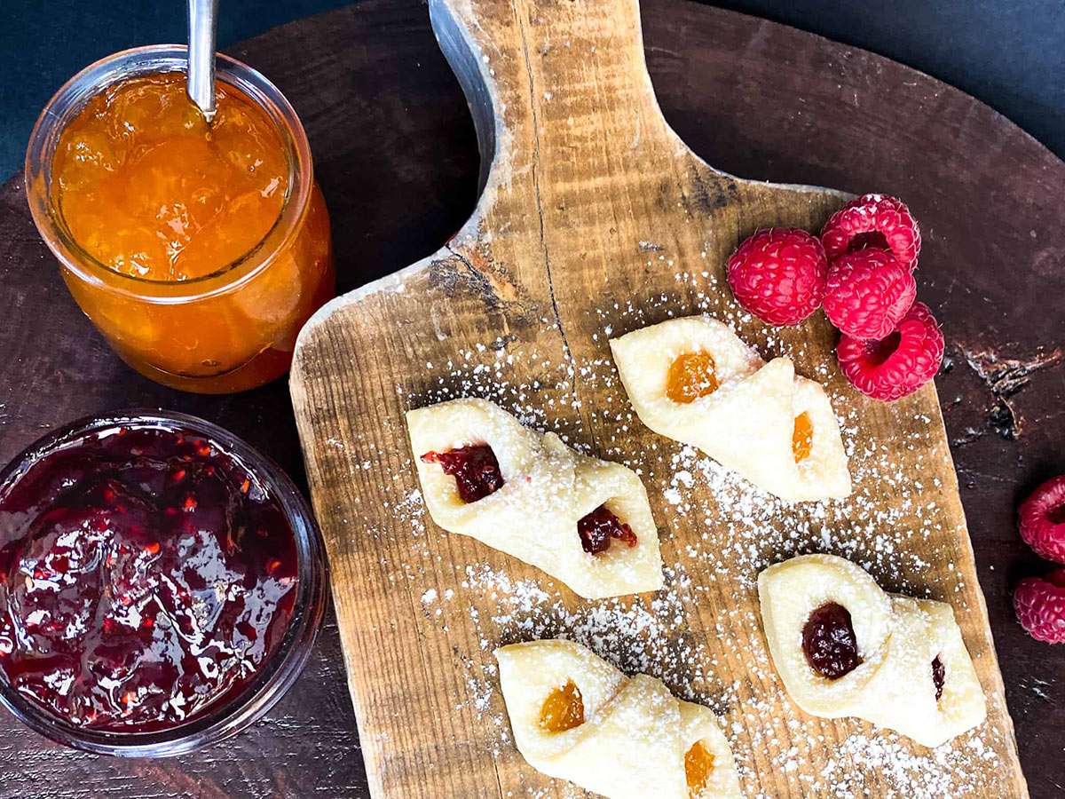 Kolaczki Cookie on a cutting board. There are two jars with jam next to it | Girl Meets Food