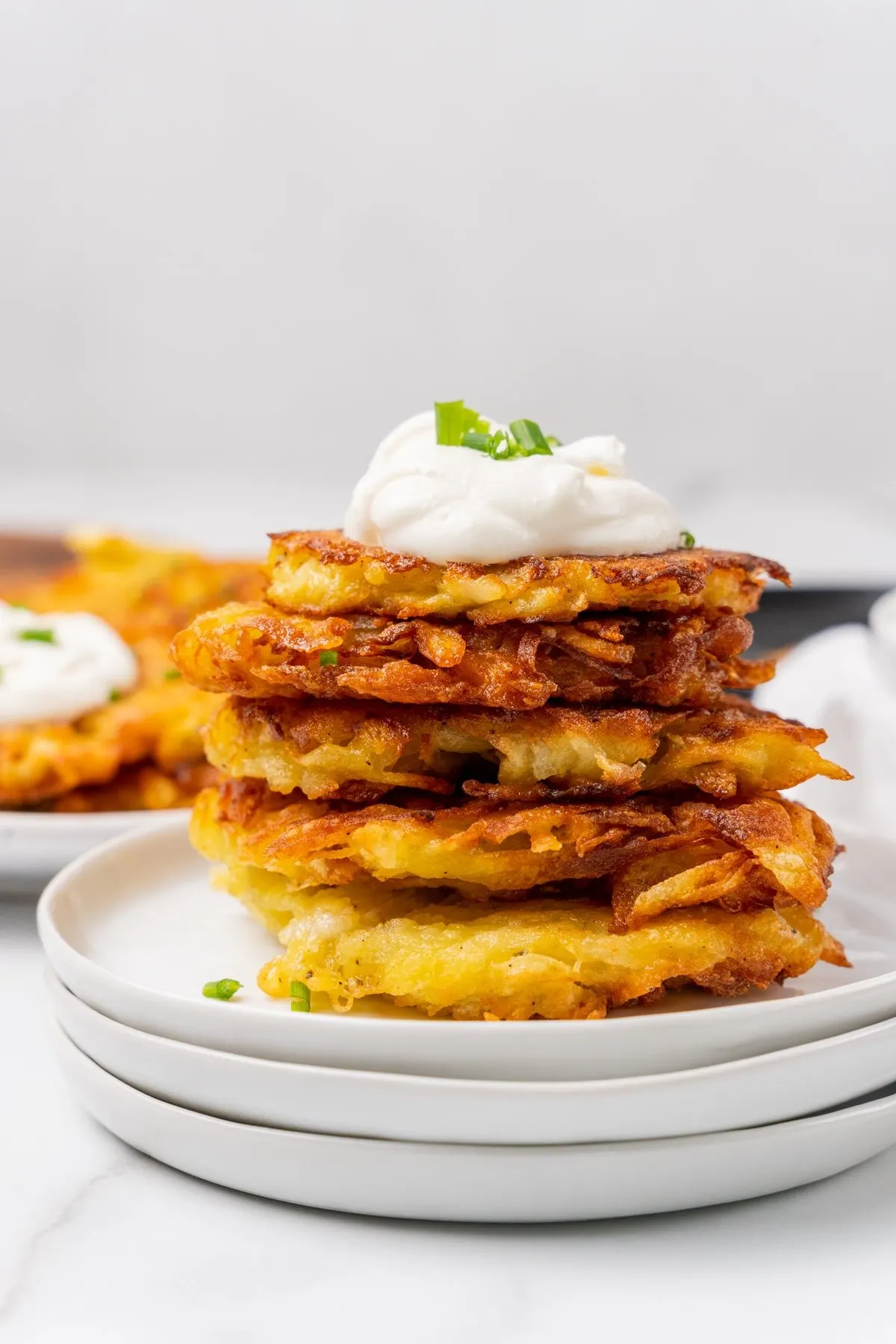A pile of potato pancakes topped with sour cream on a plate | Girl Meets Food