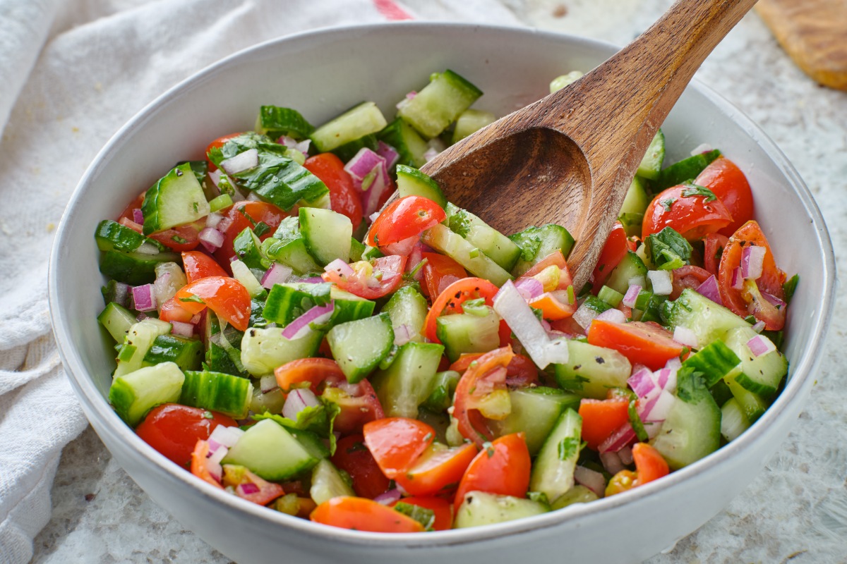 A bowl of cucumber tomato onion salad with a wooden spoon | Girl Meets Food