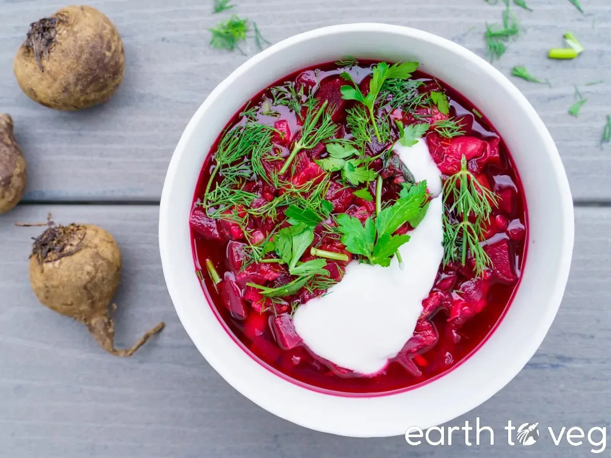 A bowl of Vegan Borshch and two beets on the table | Girl Meets Food