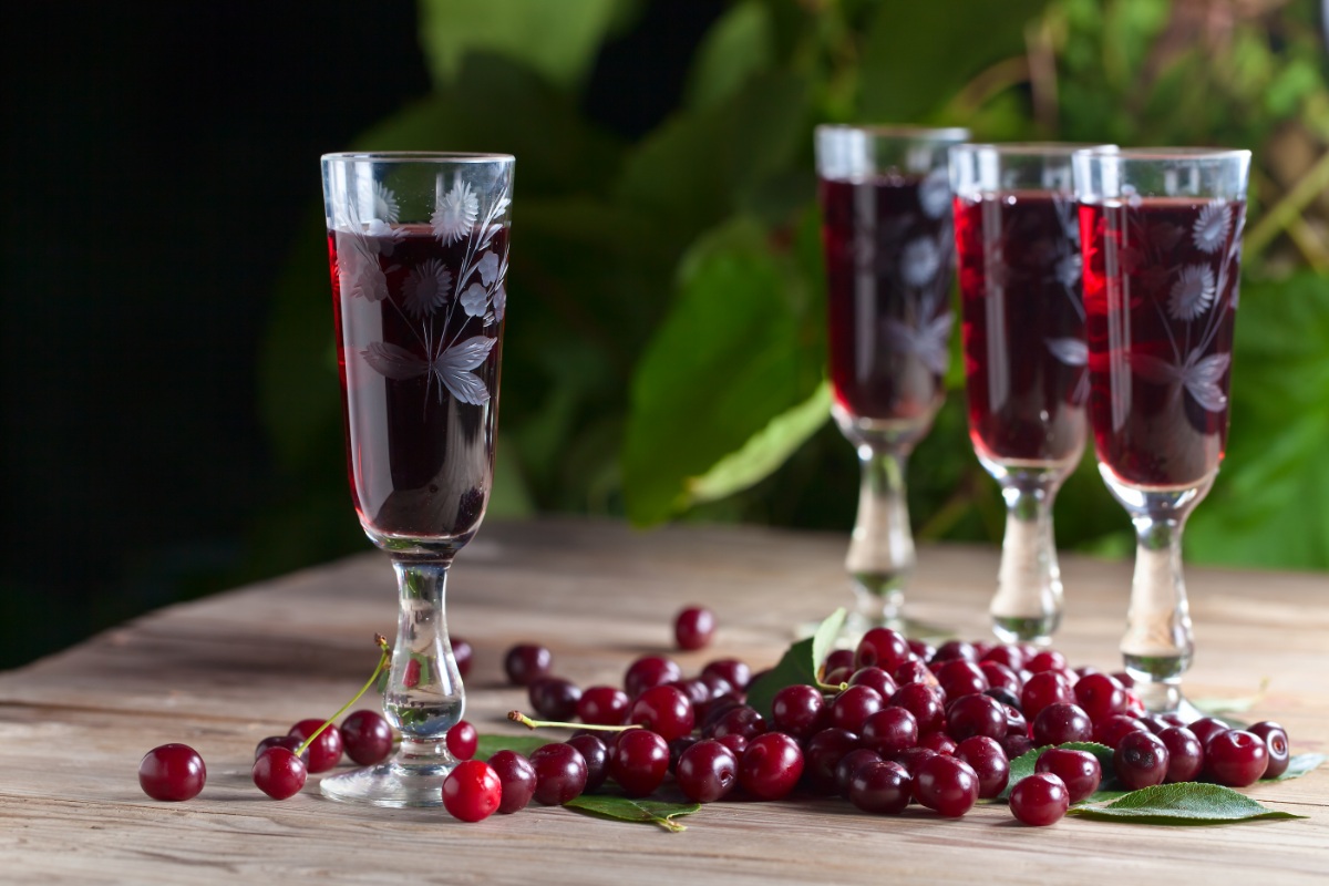 Four glasses of Wisniówka (cherry liqueur) on the table. Cherries are scattered around the glasses | Girl Meets Food