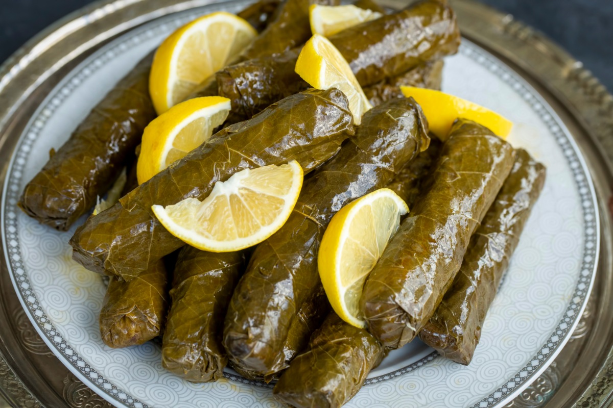 A plate of Sarmi (Stuffed Grape Leaves) topped with lemon slices on the table | Girl Meets Food